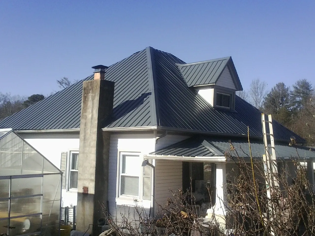 Dark blue standing seam metal roof on a white farmhouse with dormer — Slate & Tile Roof Repair by Roofing Brothers in Raymond