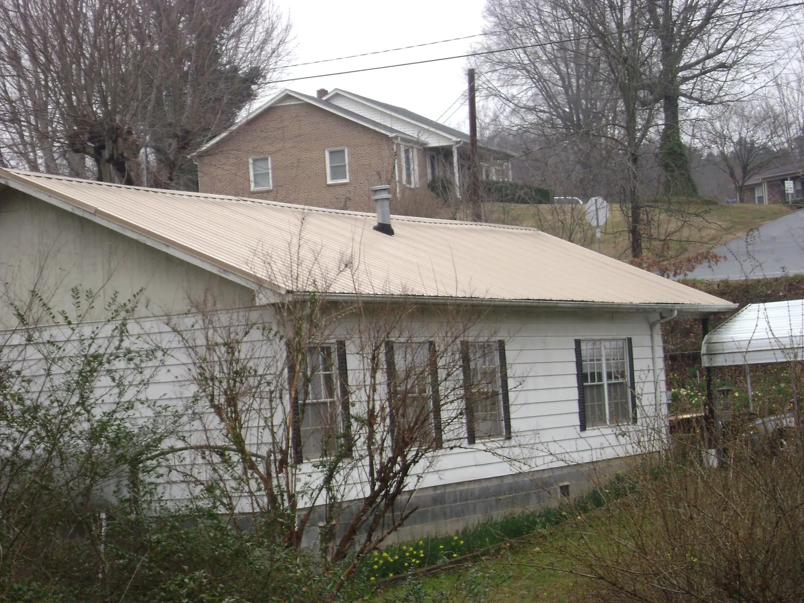 Tan metal roof on a white sided house set into a hillside — Commercial Roofing by Roofing Brothers in Raymond