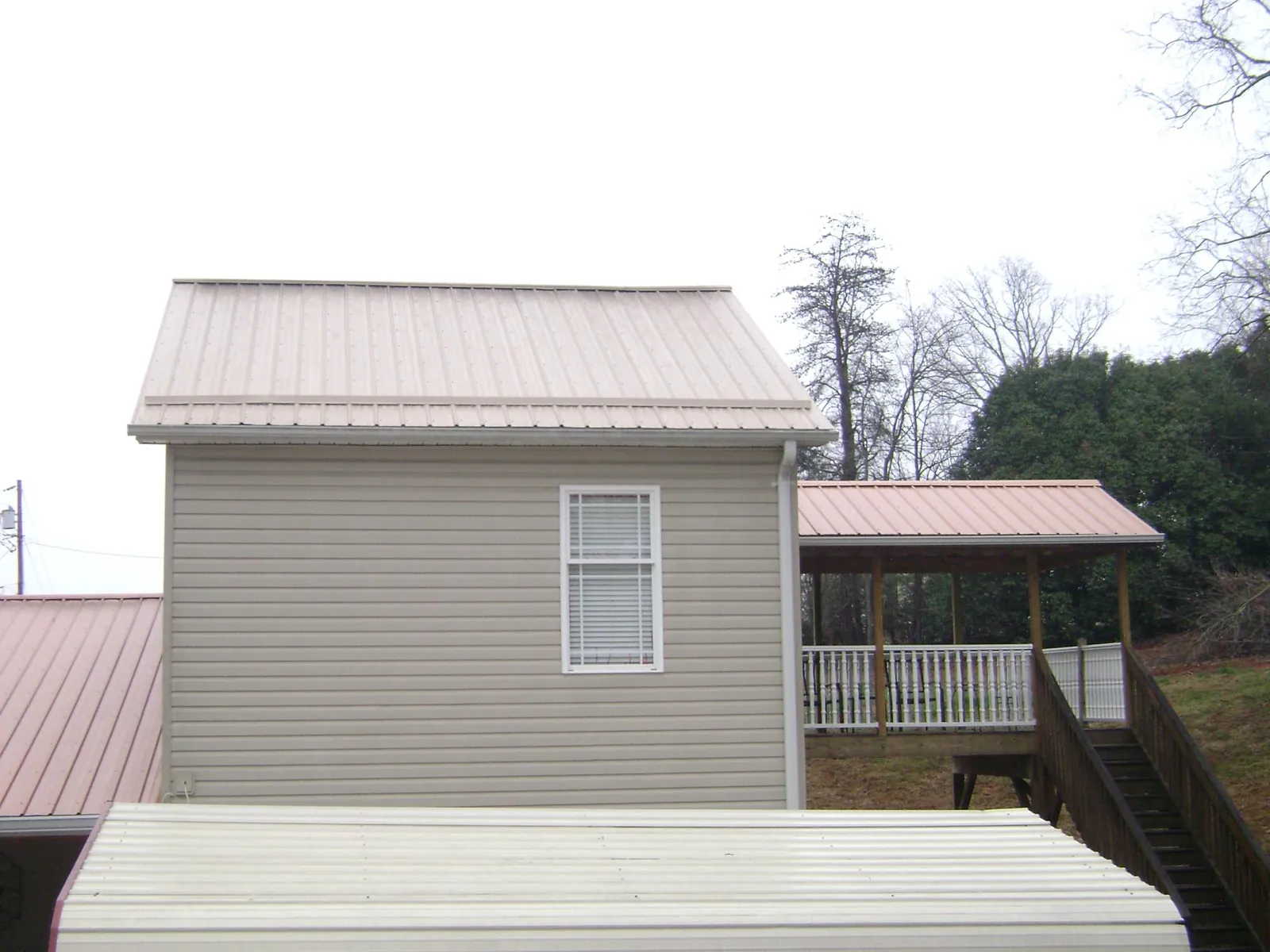 Tan metal roofs on a two story addition and attached porch, from a Roof Replacement job in Raymond
